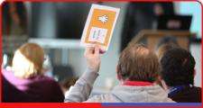 Man sitting in crowd holding up a leaflet 